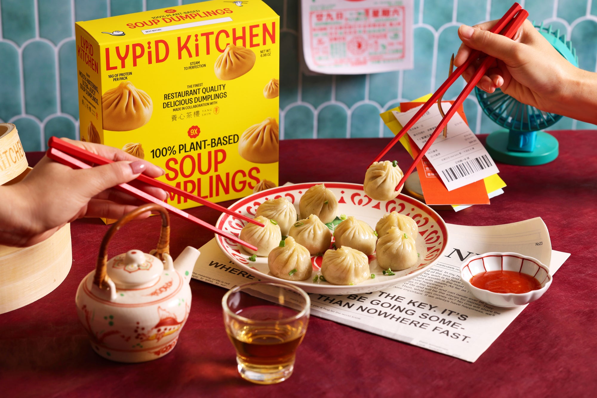 LYPID KITCHEN soup dumplings with red tongs, a teacup, and a glass of tea on a table.