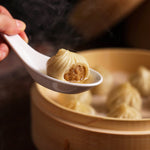 Steamed dumplings are being served with a white spoon over a bamboo steamer.