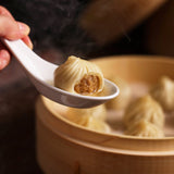 Steamed dumplings are being served with a white spoon over a bamboo steamer.