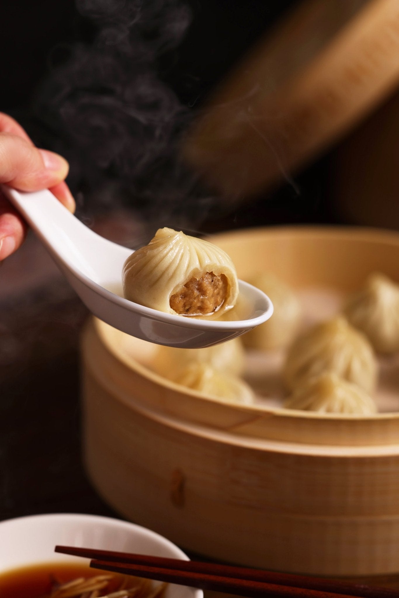 Steamed dumplings are being served with a white spoon over a bamboo steamer.
